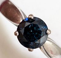 Top-down close-up of round blue diamond in six-prong white gold setting