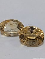 Two oval-cut citrine gemstones placed on a white background showing their color and facets from a side angle.