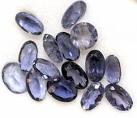 Multiple faceted iolite stones on light background showing natural color and inclusions.