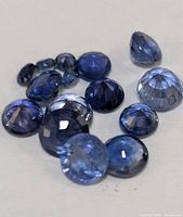 Close-up photo showing a group of 13 loose genuine sapphires, all blue and faceted in various cuts and sizes.