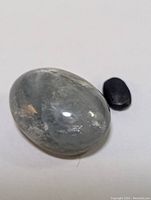 Photo showing the oval star sapphire cabochon with visible star-like reflections and a smaller dark polished stone beside it.