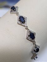 Close-up image of the bracelet showing four sapphire stones set in diamond-shaped frames with clear accent stones on a display stand.