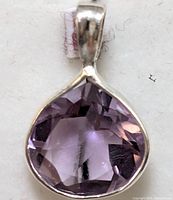 Close-up front view of a silver pendant with a faceted teardrop-shaped amethyst stone set in a bezel frame with silver bail.