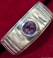 Close-up of the top view of a silver ring with a round purple amethyst set in the center, showing the textured band design and gemstone details.
