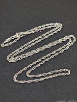 Full view of 20-inch silver rope chain necklace laid flat on a black surface.