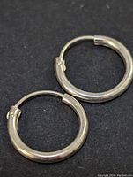 Pair of silver hoop earrings displayed on black background, showing size and clasp detail.