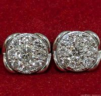 Close-up front view of two silver lab-created diamond cluster stud earrings on red background.