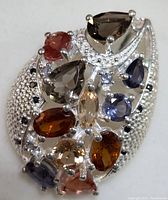 Close-up front view of silver multi-gemstone pendant showing detailed setting, multiple colored genuine gemstones in various cuts and sizes.