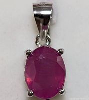 Close-up front view of silver pendant with oval faceted deep red ruby stone in four-prong setting.