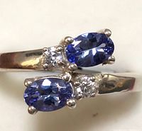 Close-up angled photo of silver ring showing two oval blue tanzanite stones with side clear round stones