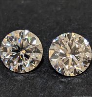 Close up image of two round moissanite stones on black surface showing facets and brilliance.