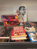 Collection of 49ers memorabilia on metal shelf including Joe Montana signed race car model in box, several books, print artwork, laminated ticket and game card.