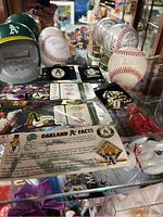 Photo showing signed baseballs, pins with 'A's Brand' logo, laminated tickets, mascot card, and baseball helmet clock.