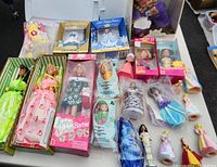 Wide view of mixed Barbie and other dolls collection including boxed and loose items laid out on table.
