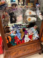 Glass case with multiple Beanie Babies including some in protective acrylic cases on top shelf and many loose on bottom shelf.