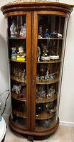 Full front view of curved wood curio cabinet with glass doors showing six shelves containing various decorative items