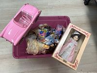Pink plastic tub containing multiple dolls in clothing and a pink Corvette toy car on side of tub. Vintage Ideal doll in pink lace dress and original box leaning on tub.