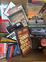 Box of assorted DVDs with visible titles including The 2000 Year Old Man, The Vietnam War, and others in various condition.