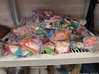 Shelf filled with a large number of sealed Happy Meal toys in plastic packaging from McDonald's, covering multiple characters and series.