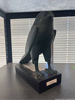 Front left angle view of black and green Horus falcon statue on base showing the bird's head, claws, wing details, and 'Horus' label on base.