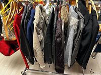 Photo showing 8 ladies jackets and coats on hangers, displayed side by side showing various styles and colors including black, beige, grey, and red.