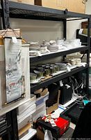 Full view of large black metal shelving unit holding various household items, showing four metal grate shelves and sturdy metal frame.