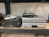 Photo of five media players on a shelf including Sony VHS player, two Panasonic DVD players, a Coby DVD player, and a Pioneer electronic device.