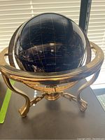 Front and side views of the dark blue lapis globe showing the South Pacific and surrounding regions with gold geographic details, mounted on a brass tripod stand with armillary ring.