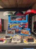 Three racing team baseball caps and various packaged model cars on wire shelving