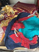 Close-up photo showing two silk scarves: one burgundy with gold ornate pattern and one multicolored with navy, turquoise, red and pearl-like motif folded on top.