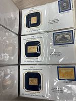 Close-up of three golden replica stamps including 1861 George Washington 24¢, 1888 Trans-Mississippi Exposition 10¢ Handclasp of Emigration, and 1912-3 Panama-Pacific Exposition 10¢ Discovery of San Francisco Bay.