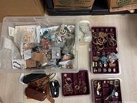 Overview of plastic bin containing mixed costume jewelry, multiple jewelry trays, and jar with loose items, with glasses cases seen around.