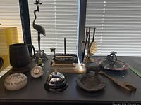 Full view of lot items on black desk surface including brass crane statue, desk accessories, ashtrays, and brass animals