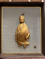 Full view of gilded child wall relief mounted in wooden frame with gray textured fabric and gold border.