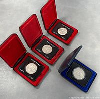 Four Canadian commemorative coins in their original presentation cases placed on a grey surface, three red cases and one blue case, showing front views of the coins.
