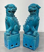 Pair of porcelain turquoise Foo Dogs showing front and side profiles on square bases.