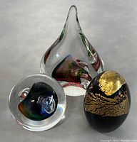 Group photo showing all three glass pieces: two paperweights and one decorative egg