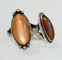 Two vintage sterling silver rings side by side, showing elongated oval orange and brown cabochon stones with silver settings and bands.