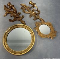 Photo showing two gold vintage wall sconce candle holders and two gold framed mirrors, one round and one ornate.