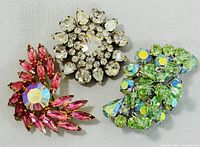 Front view showing three rhinestone brooches: pink swirl with AB stone, clear rhinestone round brooch, and green-blue cluster brooch.