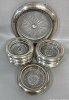 Seven sterling silver round bottle coasters with one glass coaster with sterling silver rim, all with minor wear and tarnishing.