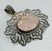 Front angle of the rose quartz gemstone cabochon pendant with detailed silver floral openwork design.