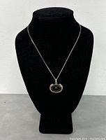 Front view of the necklace displayed on a black bust, showing the silver chain and the oval smokey quartz pendant.
