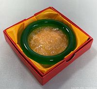Natural green jade bangle in a red box with yellow satin lining and bubble wrap cushioning.
