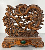 Frontal close-up of the carved boxwood Chinese dragon and ruyi screen showing the detailed dragon scales and cloud motifs along with the green oval gem on the wood base.