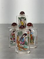 Set of four hand-painted Chinese glass snuff bottles closely grouped showing detailed painted figures and reddish stoppers