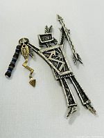 Close-up front view of signed 925 silver brooch shaped like an abstract figure holding an arrow with bead and arrow-shaped charms hanging.