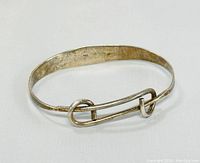 Vintage silver bracelet shaped like a safety pin, shown at an angle revealing the clasp and overall design.