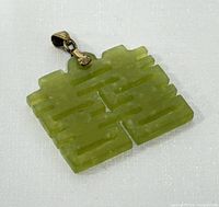 Front view of the carved green jade happiness pendant showing the intricate geometric design and attached metal bail.
