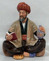 Front view of Royal Doulton Omar Khayyam figurine showing detailed face, red turban, beige robe, brown pants, holding book and jug.